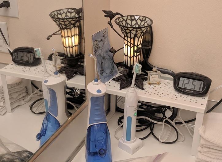 Elektrické zubné kefky a lampička na poličke vedľa zrkadla v kúpeľni, ukazuje presný čas.