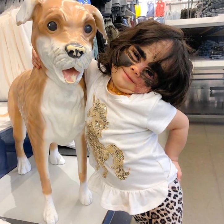 Dievčatko v bielej košeli s leopardím vzorom stojí vedľa sochy psa v predajni.