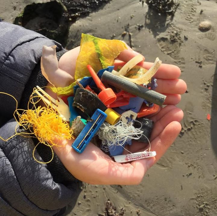 Ruky držia rôznofarebný plastový odpad na piesočnatej pláži. Ekologická téma a znečistenie oceánov.