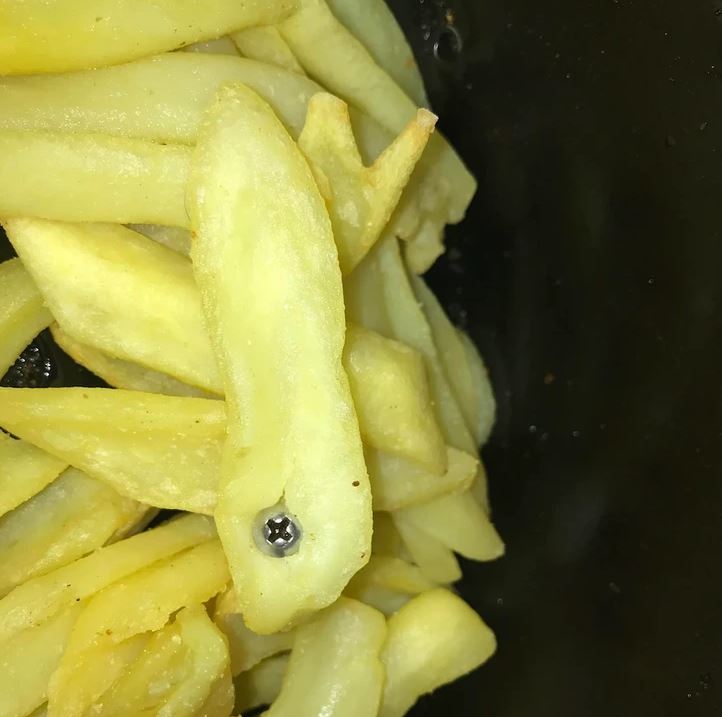 Hranolky s kúskom hranolky v tvare ryby, v strede s čiernou škvrnou, na čiernom pozadí.