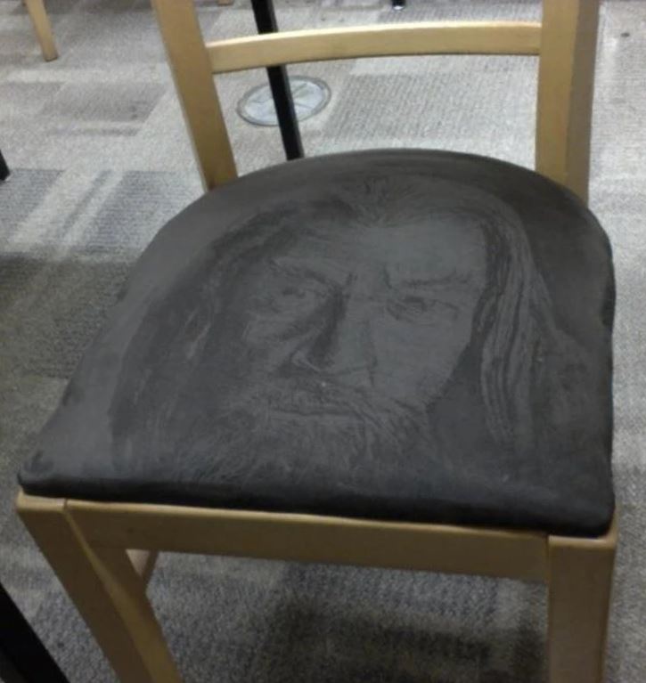 Stolička s prachovým obrysom tváre na sedadle, originálne umenie na kancelárskej stoličke.