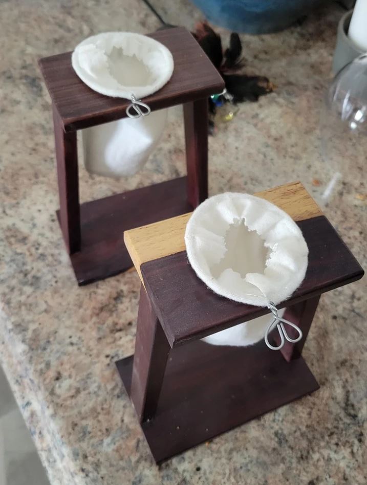 Dva drevené stojany s bielymi textilnými filtrami na prípravu kávy na kuchynskej doske.