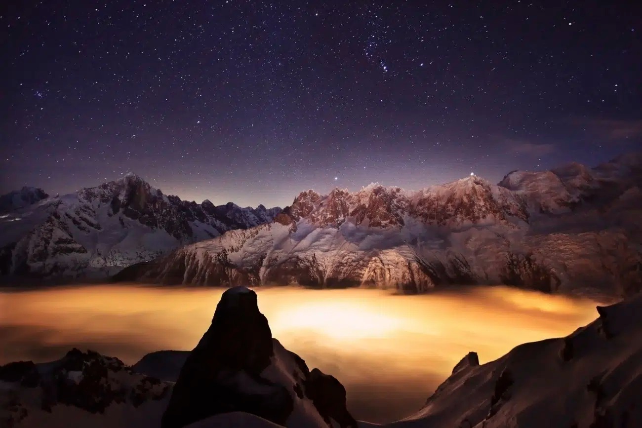 Hory za súmraku s hviezdami na oblohe a zlatou hmlou pod vrcholmi.