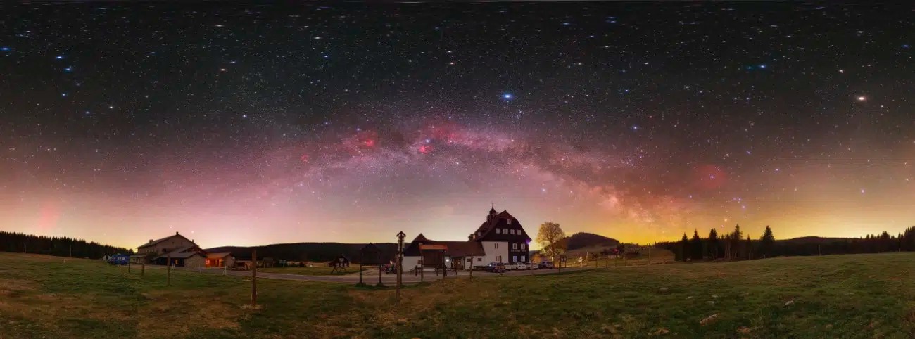 Mliečna dráha nad nočnou krajinou s domom a hviezdnou oblohou na vidieku.