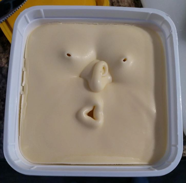 Tvar masla s podobou tváre v plastovom obale, vytvára unikátny a zábavný dojem.