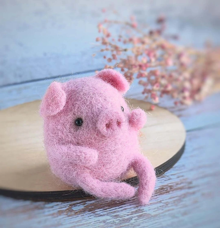 Ružové plstenné prasiatko na drevenom podnose s jemným ružovým kvetinovým pozadím.