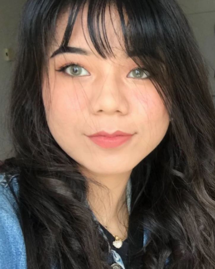 Osoba s dlhou tmavou vlasovou ofinou a jemným make-upom, oblečená v džínsovej bunde.