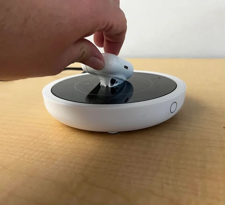 Ruka drží bielu myš na čiernej bezdrôtovej nabíjačke na drevenom stole.