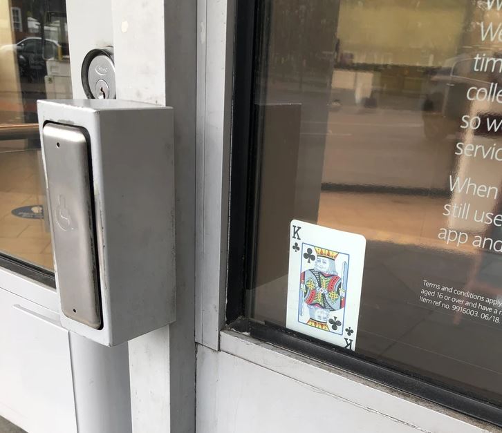 Hracia karta, kráľ kríž, zasunutá v ráme dverí vedľa tlačidla na otváranie pre vozíčkarov.