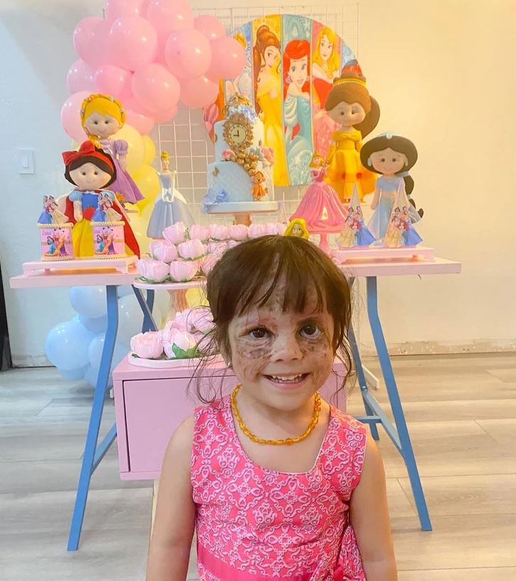 Oslava s princeznovskou výzdobou: dievčatko v ružových šatách pred dekoráciou s balónmi a hračkami.
