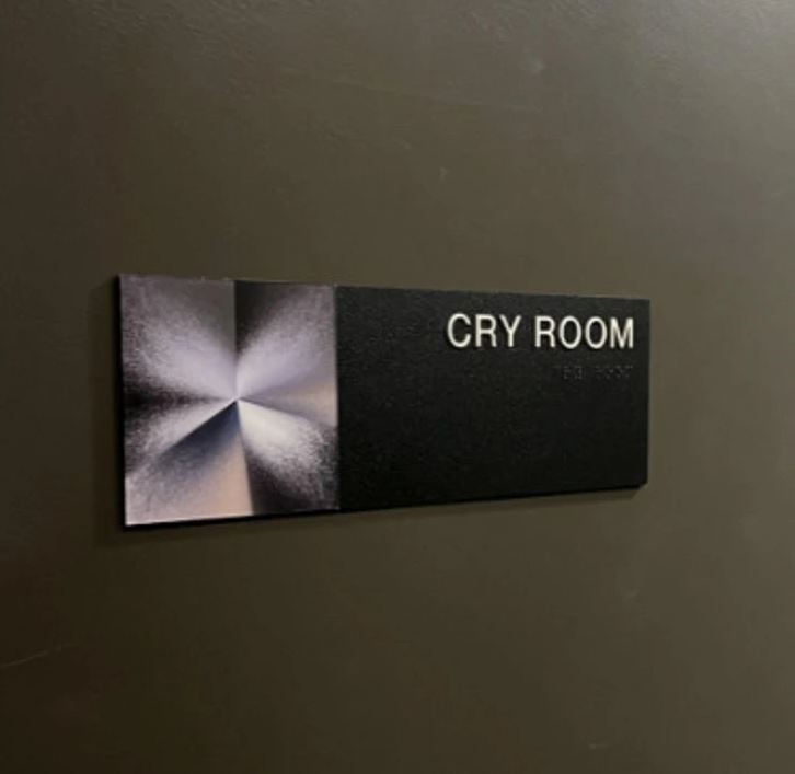 Štítok na stene s nápisom Cry Room, označujúci miestnosť na relaxáciu či úľavu od stresu.