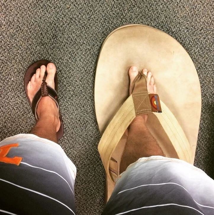 Dve nohy v sandáloch, jedna obyčajná, druhá obrovská, na koberci.