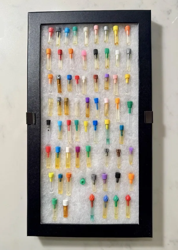 Rôznofarebné flakóny v rámčeku, organizované na textilnom podklade, zobrazené na bielej ploche.