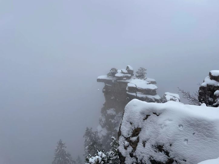 Snehom pokrytá skalná formácia v hmle, zimná krajina a hustá atmosféra na vrchole hory.