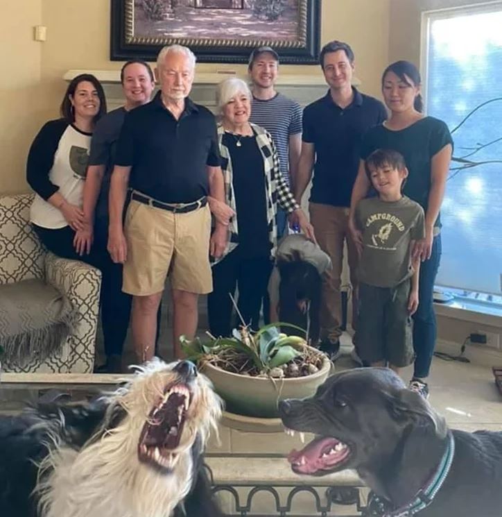 Rodinná fotografia v obývačke so šťastnými ľuďmi a dvoma psami hrajúcimi sa v popredí.