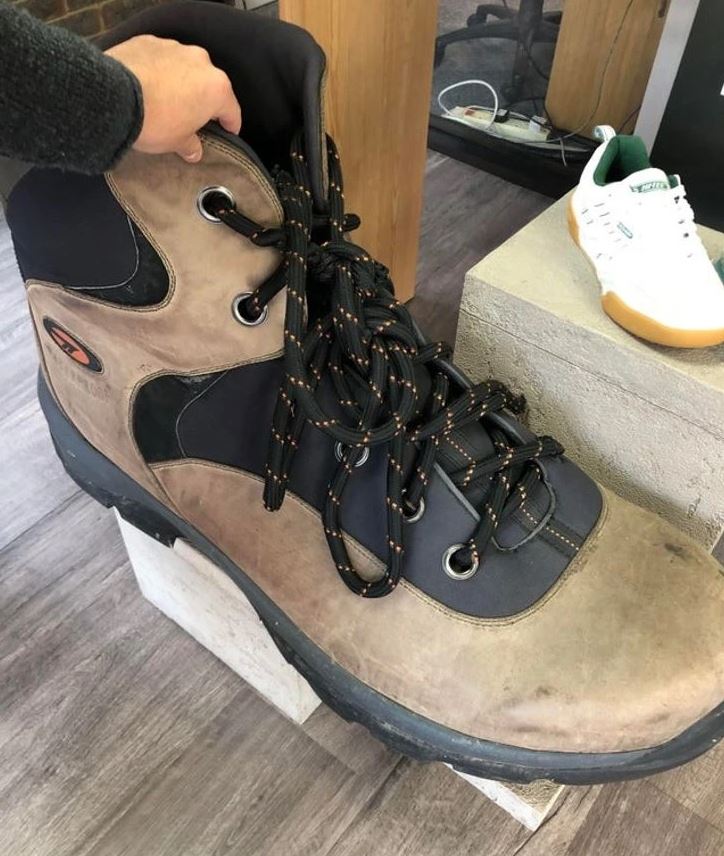 Veľká turistická topánka na stojane s rukou, ktorá ukazuje jej veľkosť; biela teniska v pozadí.