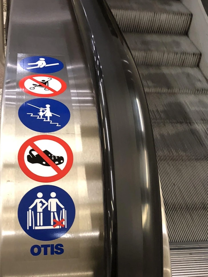 Bezpečnostné piktogramy na pohyblivom schodisku: žiadne sedenie, kočíky, šľapky, státie na okraji. Značka: Otis.
