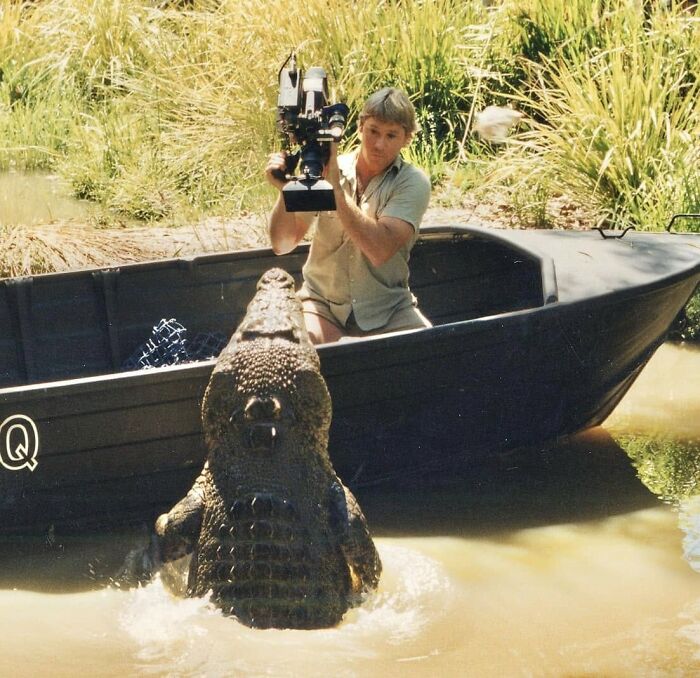 Osoba na člne fotografuje krokodíla vo vode, pričom krokodíl zdvihol hlavu nad hladinu.