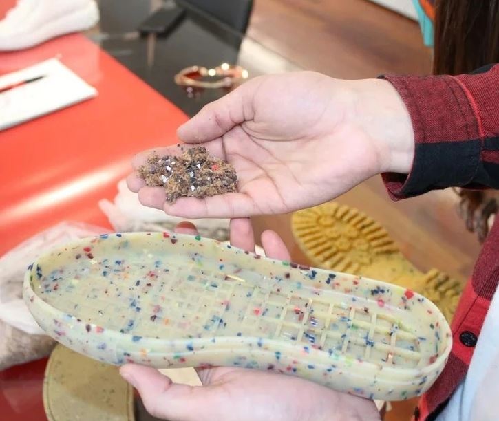 Osoba drží podrážku topánky z recyklovaného materiálu a vzorku plastového odpadu na recykláciu.