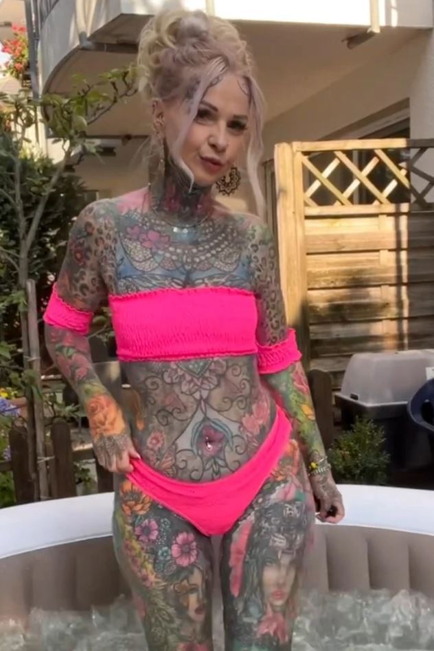 Osoba s tetovaním v ružových plavkách stojí vo vírivke na záhrade.