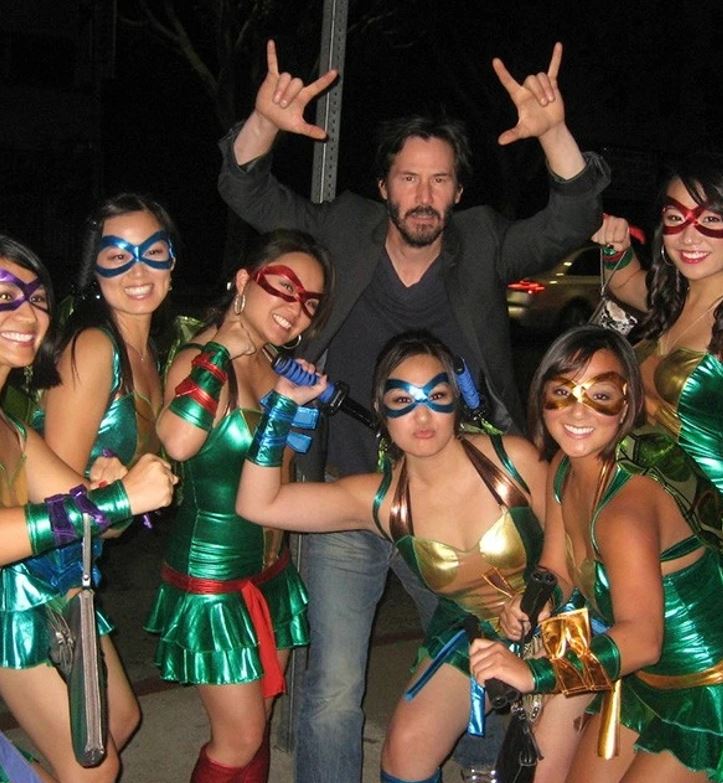 Skupina ľudí v kostýmoch ninja korytnačiek pózuje na ulici s mužom v saku.