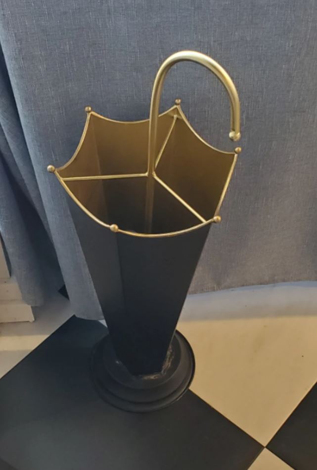 Štýlový čierny stojan na dáždniky s elegantným zlatým detailom na dlaždicovej podlahe pri záclone.