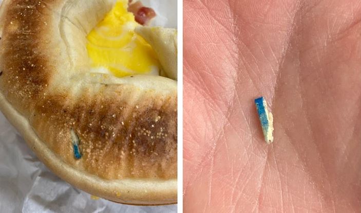 Bagel s vajcom a modrým plastovým úlomkom na ruke zákazníka – potravinová bezpečnosť.