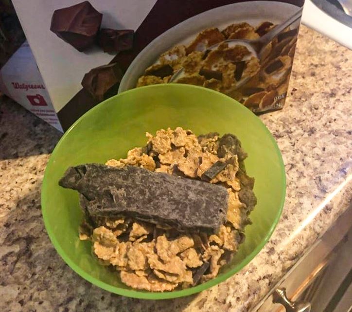 Miska cereálií s veľkým kusom čokolády na kuchynskej linke pri krabici cereálií.