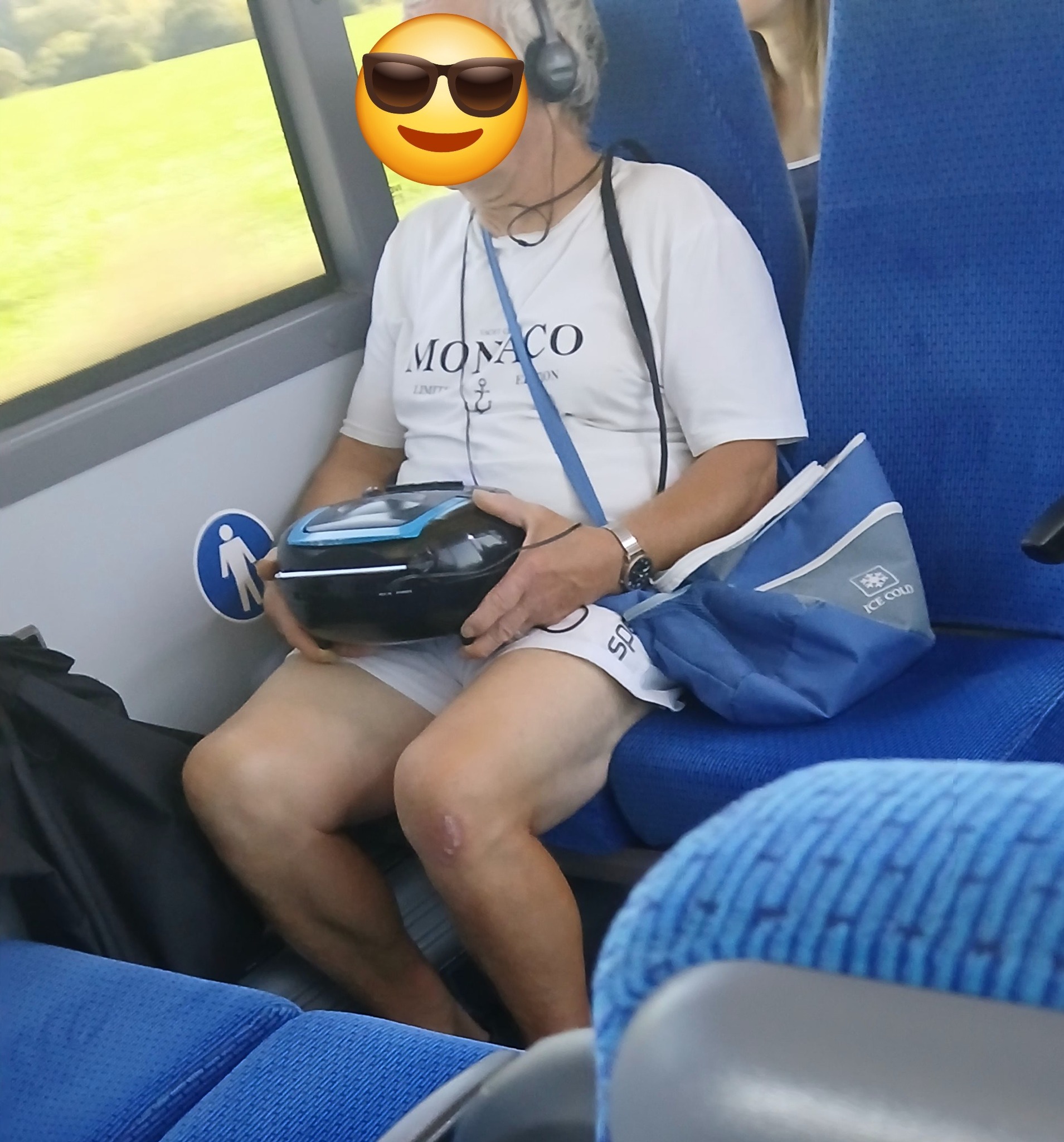 Osoba v bielom tričku s rádiom na kolenách sedí v modrom sedadle vlaku.