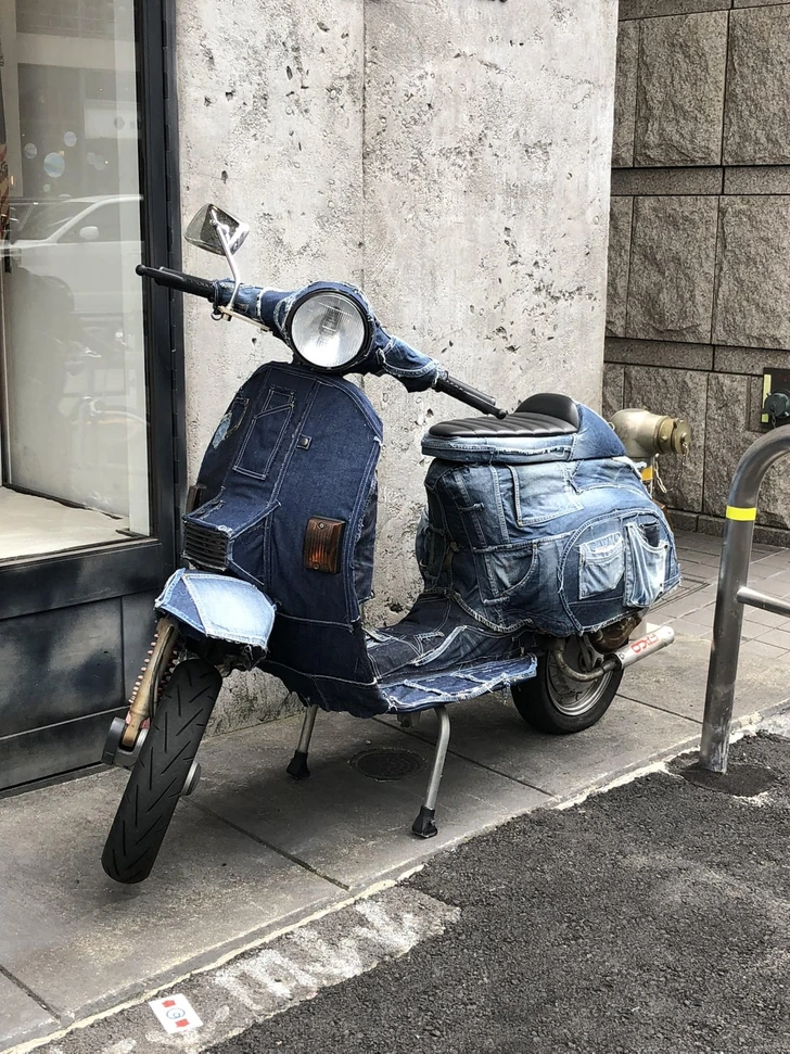 Motorka pokrytá džínsovinou zaparkovaná na chodníku pri betónovej stene v meste.