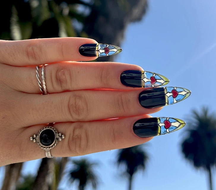 Čierne nechty s farebnými sklenenými vzormi a červeným srdcom na slnku, pri ktorom sa odrážajú palmy v pozadí.