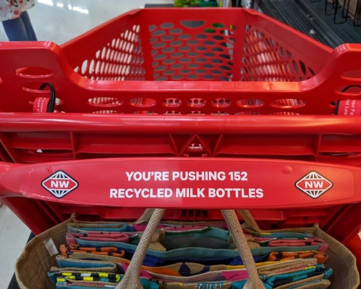 Červený nákupný košík z recyklovaných fliaš na mlieko v obchode, nápis 152 fliaš.