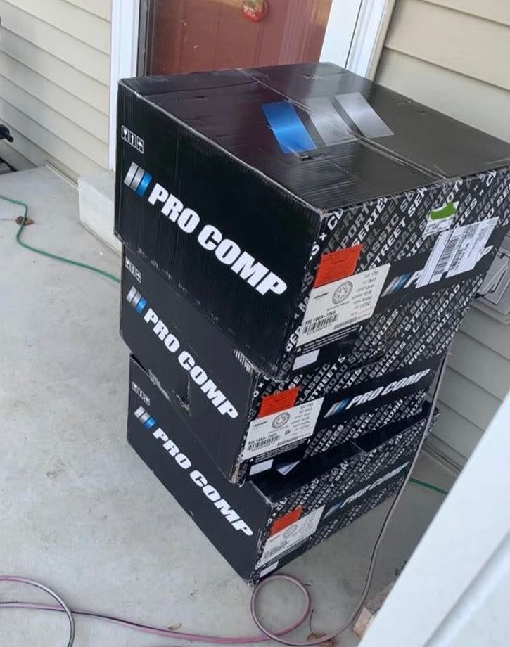 Zásielka štyroch čiernych krabíc Pro Comp na prahu pri dome.