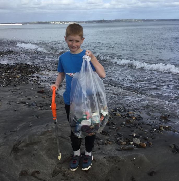 Mladý chlapec zbiera odpadky na brehu mora, prispieva k čisteniu pláže a ochrane prírody.