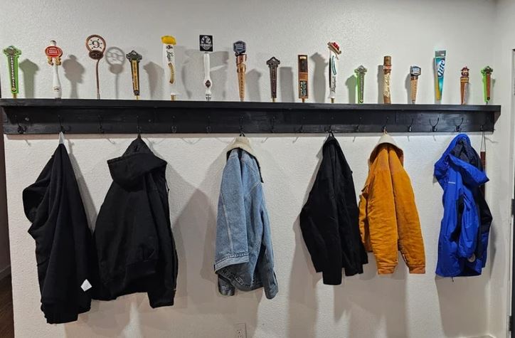 Kabáty zavesené na vešiaku s dekoratívnymi držadlami na vrchu police na bielej stene.