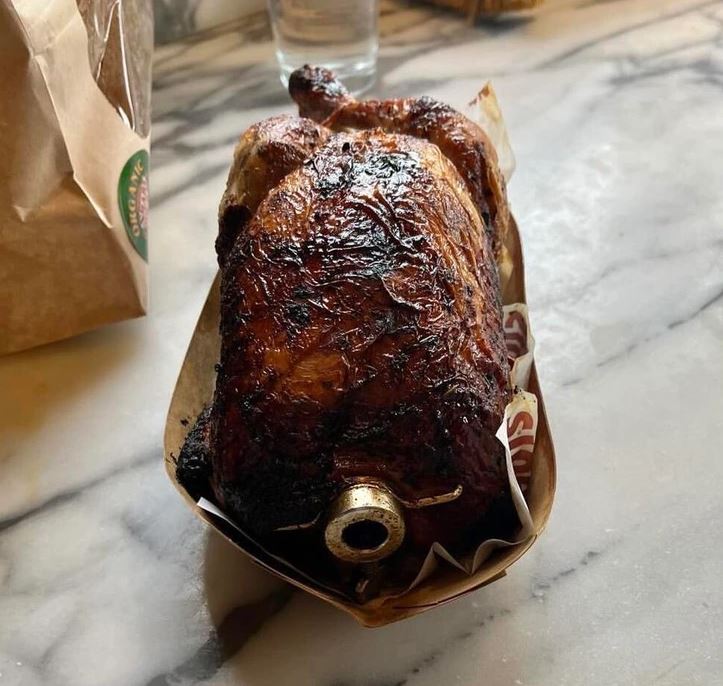 Pečené kura na otočnom ražni pripravené na servírovanie na drevenej doske.