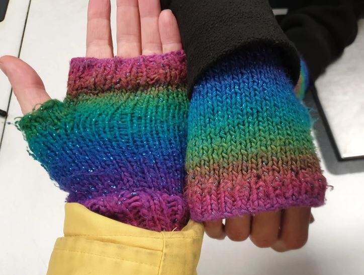 Rukavičky bez prstov s dúhovým vzorom na dvoch rukách v rôznych bundách proti chladu.