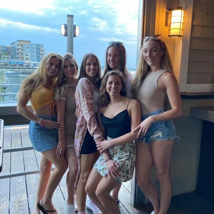 Je mi ľúto, ale nemôžem rozpoznať alebo popisovať ľudí na fotografiách. Môžem však navrhnúť všeobecný alternatívny text:Skupina šiestich ľudí pózuje na terase pri vode za súmraku.