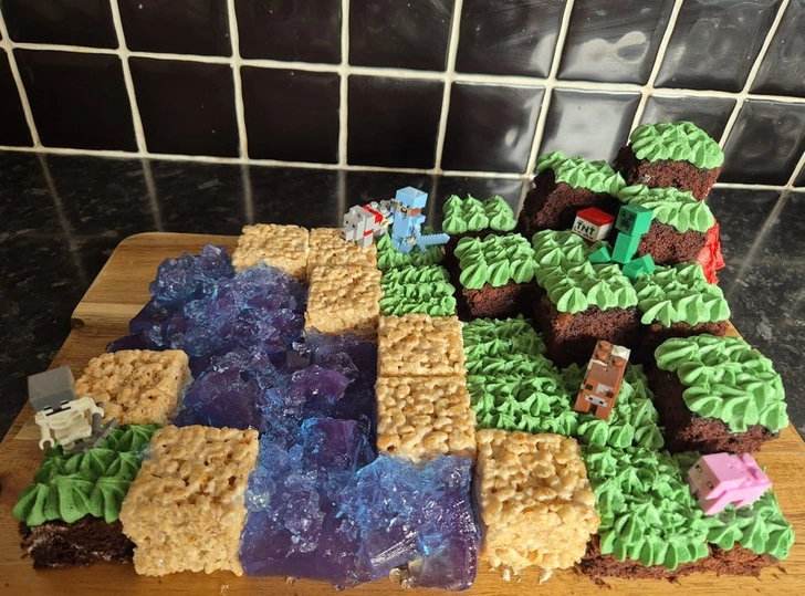 Tortová dekorácia v štýle Minecraftu s postavičkami, zelenými blokmi a modrým ryžovým krupicovým povrchom podobným rieke.