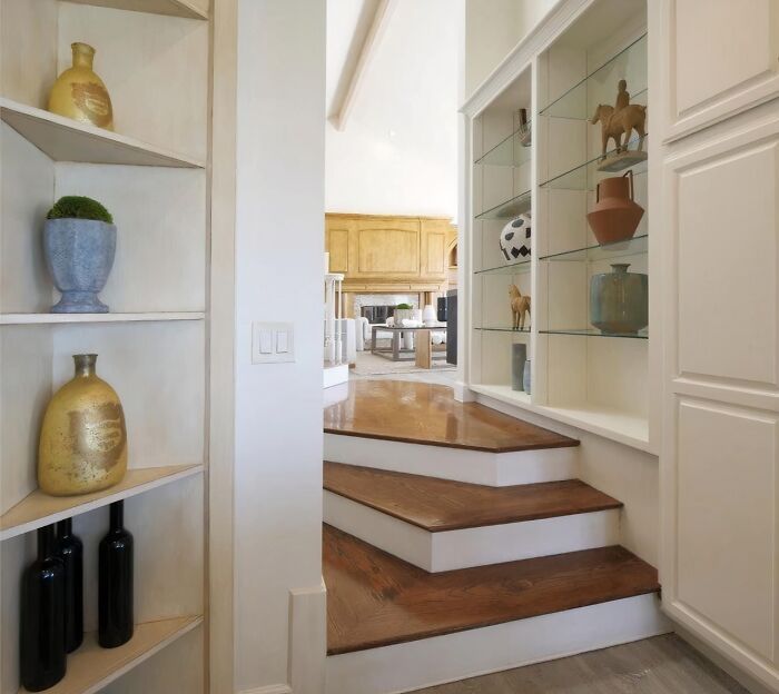 Schody vedúce do modernej obývačky s drevenými a sklenenými regálmi plnými dekoratívnych predmetov.