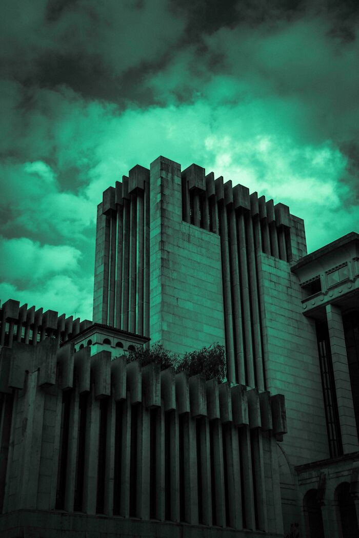 Brutalistická architektúra moderného výškovej budovy pod zeleno-tyrkysovou oblohou s hrozivými mrakmi.