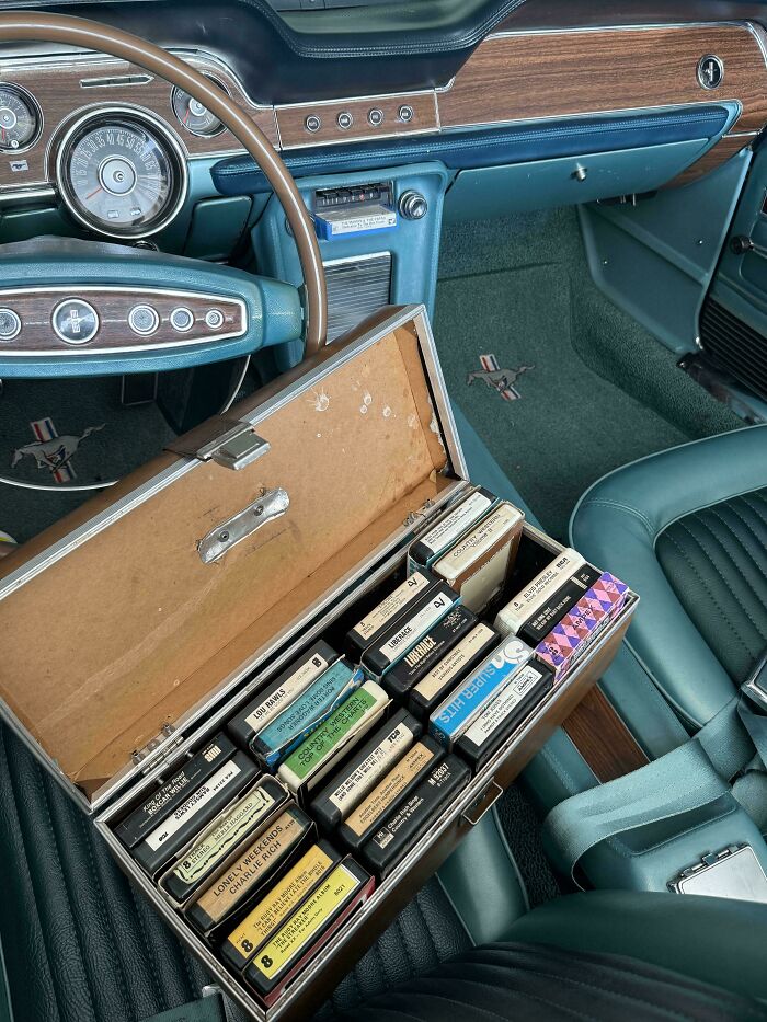 Staré autorádio s kazetami v retro aute; interiér s drevenými detailmi a koženými sedadlami.