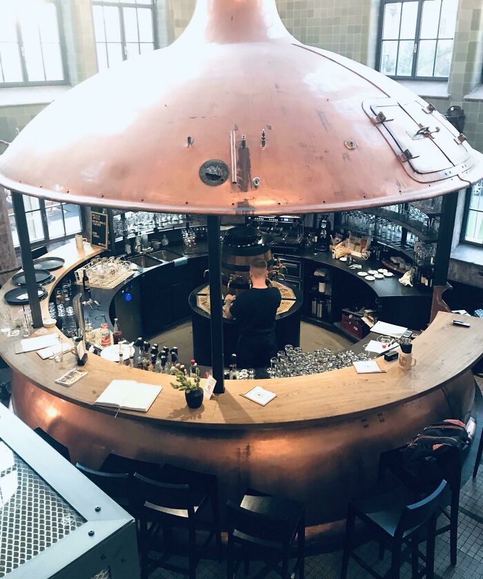 Pohľad zhora na okrúhly bar so stropom v tvare medeného kotla, kde barman pripravuje nápoje.