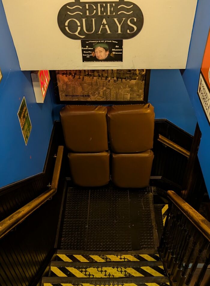 Schody s hnedými vankúšmi na stenách pod nápisom Dee Quays, modro-biele prostredie, bezpečnostné pásy na schodoch.