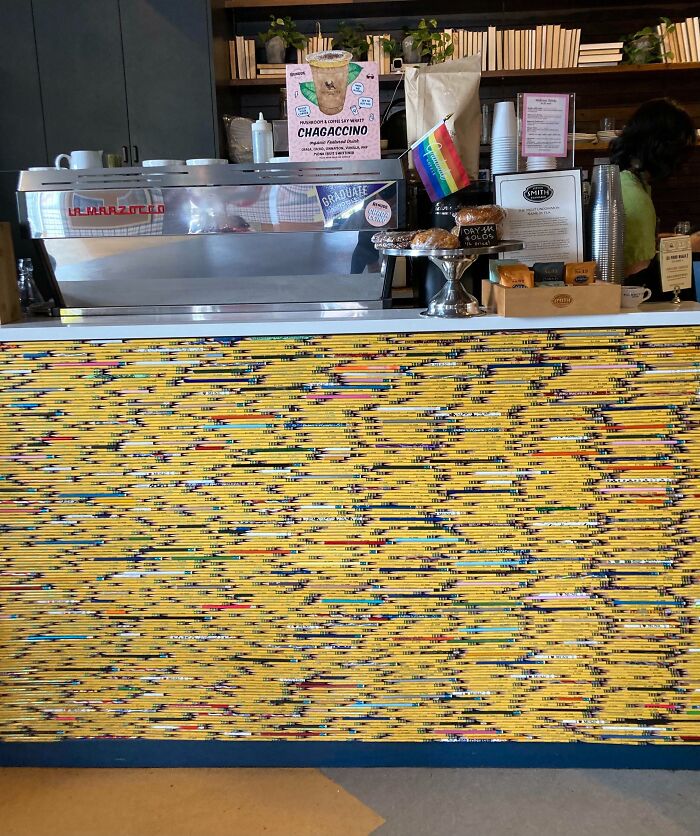 Kaviareň s kávovarom, farebná predná stena z ceruziek, dúhová vlajka a ponuka Chagaccino na pulte.