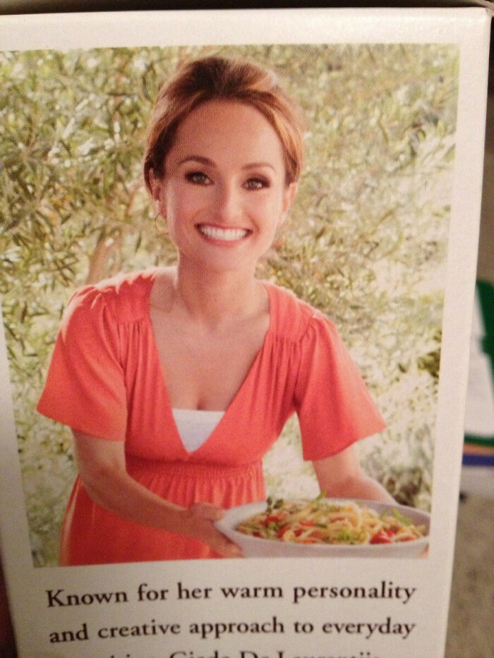 Osoba v oranžových šatách s úsmevom držiaca tanier cestovín vonku, obklopená zeleným pozadím.