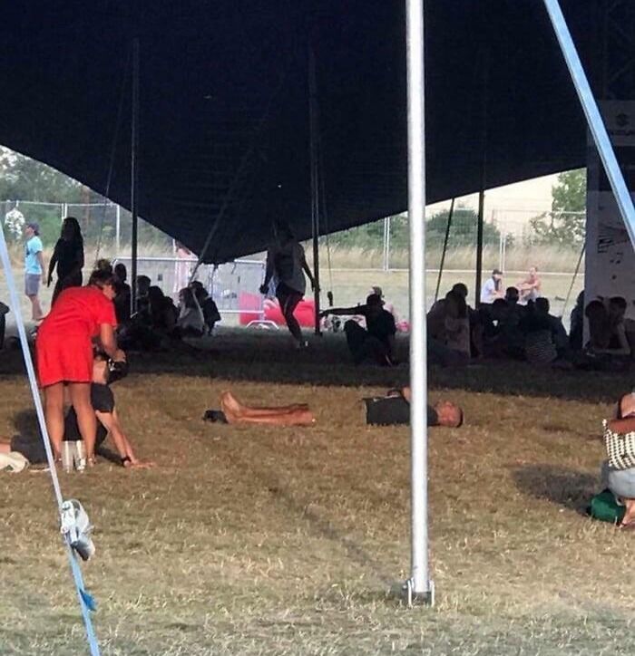 Ľudia oddychujúci v tieni veľkého stanu na letnom festivale.