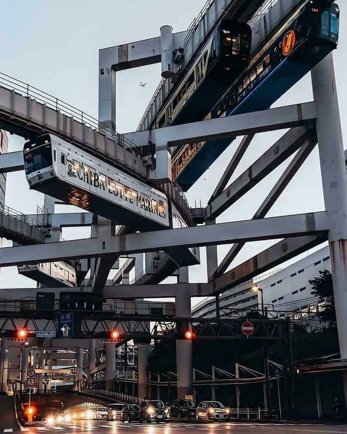 Moderná visutá železnica prechádzajúca ponad premávku na križovatke v meste, futuristická infraštruktúra.