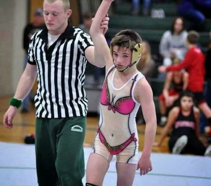 Neznámy zápasník víťazí v zápase; rozhodca zdvíha jeho ruku na znak triumfu na športovom podujatí.