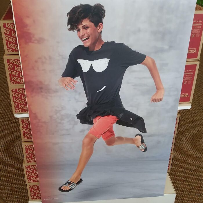 Mladík v čiernom tričku s okuliarmi a oranžových šortkách beží v predajni značky Vans s úsmevom na tvári.